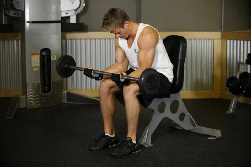 Wrist curl met barbell zittend op je bovenbenen, eindpositie